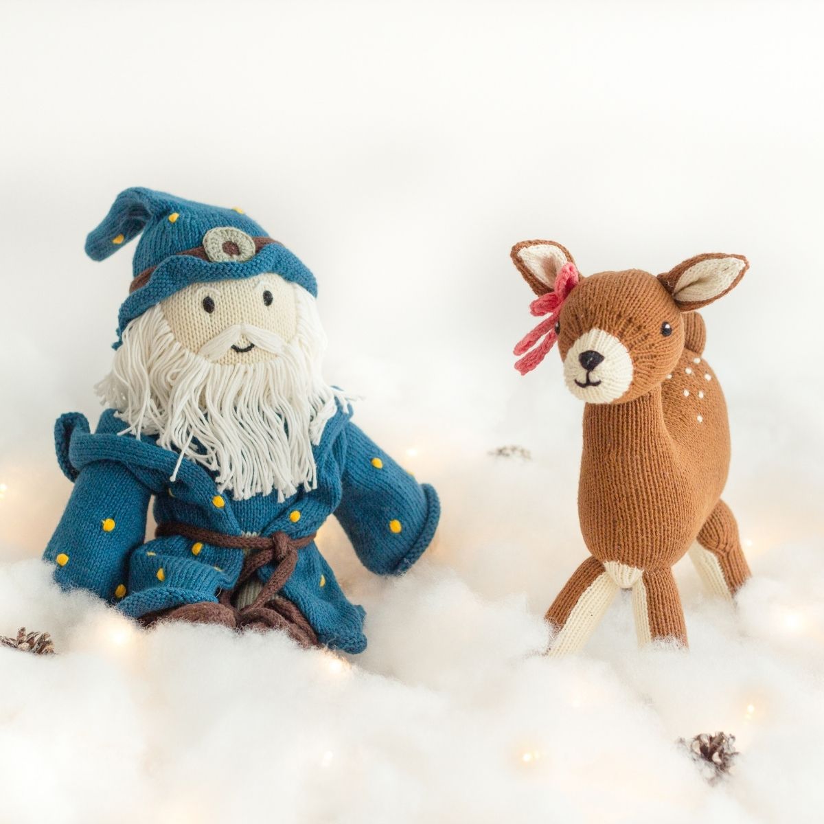 Nachhaltige Weihnachtsgeschenke für Kinder: Handgestrickter Zauberer und Reh aus Bio-Baumwolle auf winterlicher Schneelandschaft.
