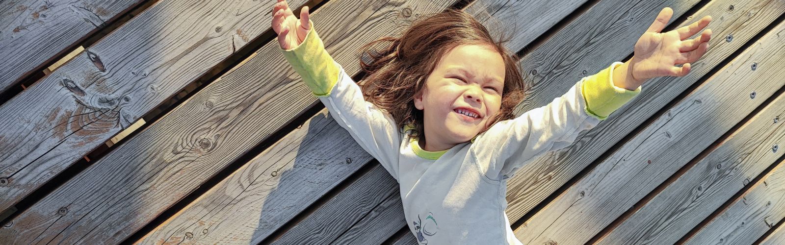 Neurodivergenz im Alltag: Ein Kind liegt entspannt mit ausgebreiteten Armen auf Holz und reguliert sich sensorisch selbst.