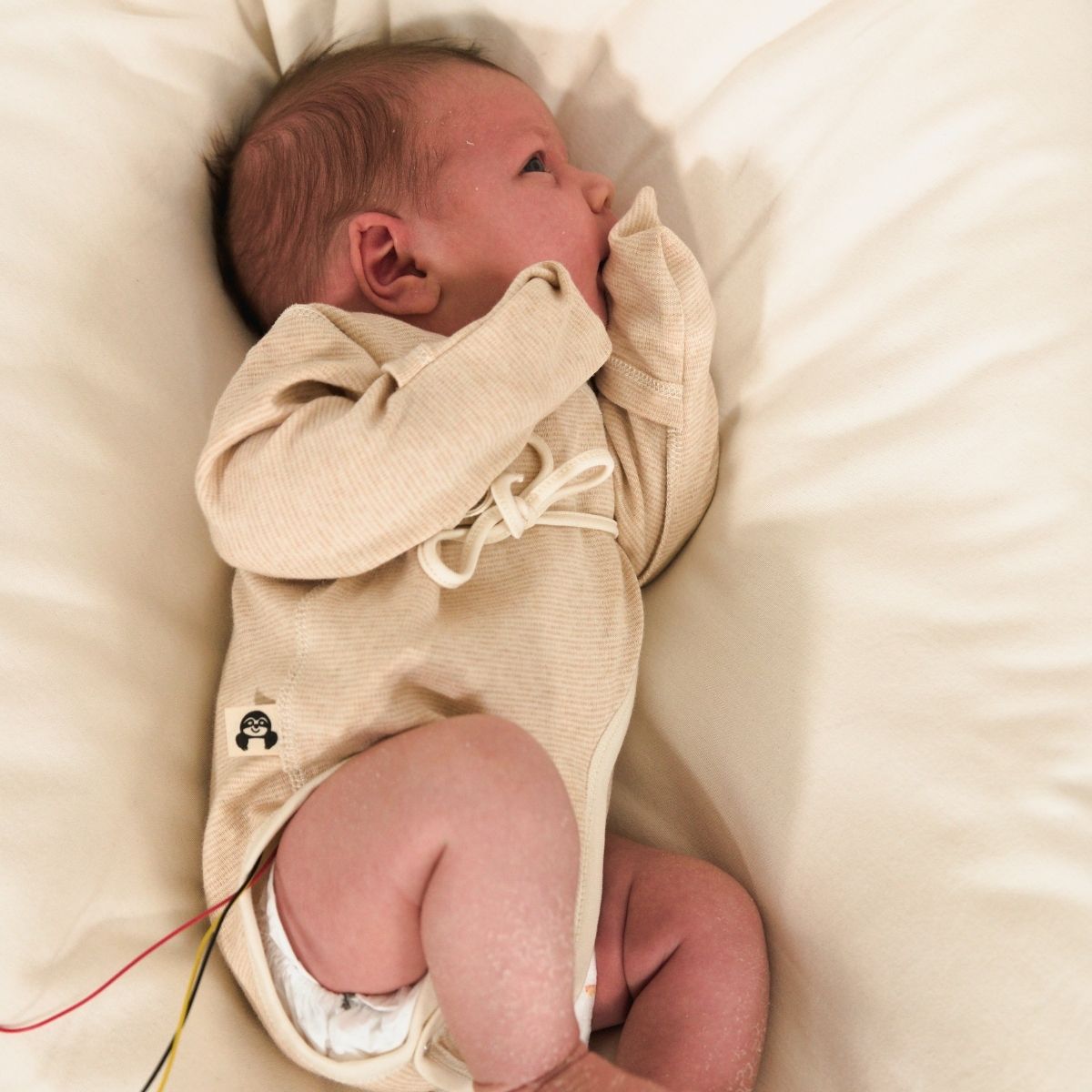 Frühchen liegt entspannt in weicher Bio-Kleidung im Bett – sicher und geborgen