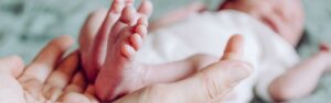 Hände halten die Füßchen eines Frühchens – Symbol für Nähe, Schutz und Geborgenheit