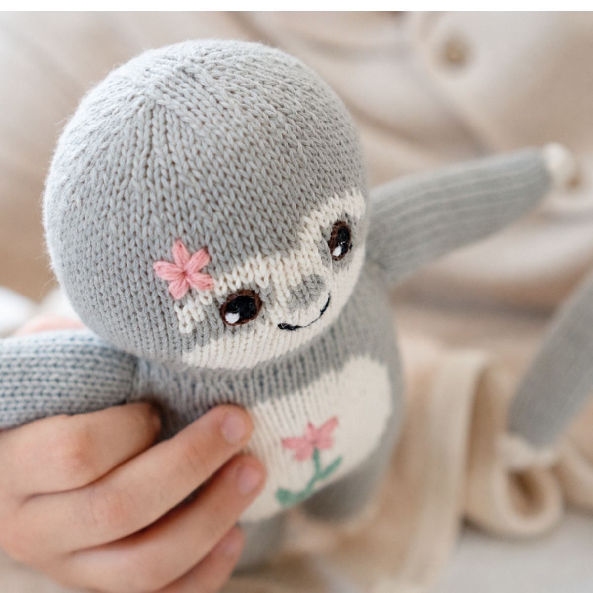 Kind hält das Baby Faultier Blumen-Fauli aus Bio-Baumwolle mit rosa Blütenstickerei