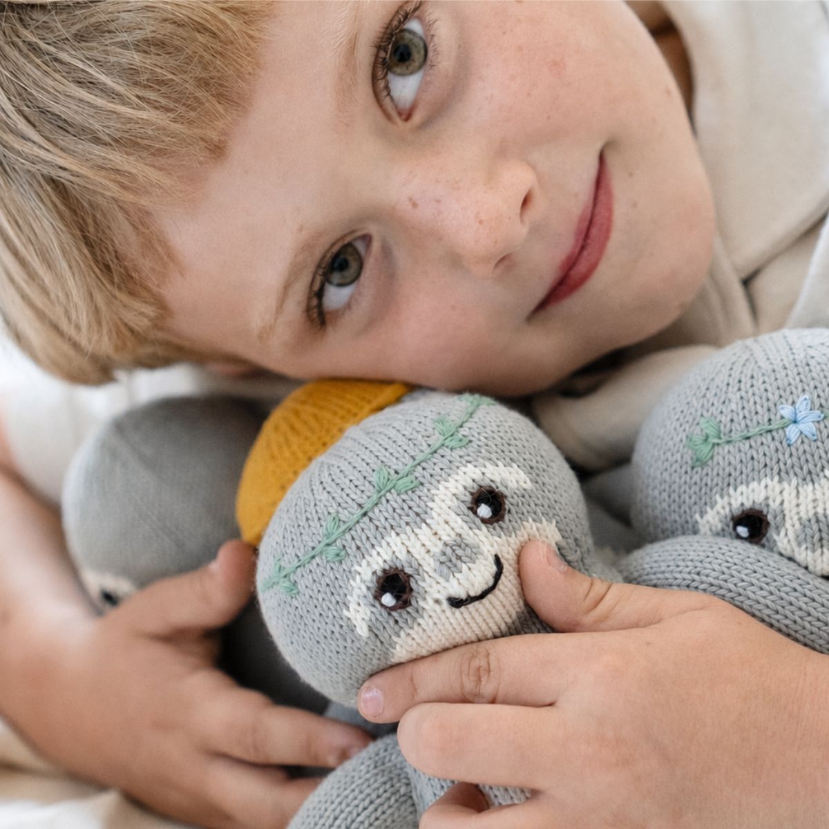 Kind kuschelt mit dem Baby Faultier Natur-Fauli aus Bio-Baumwolle mit grüner Blätterranke