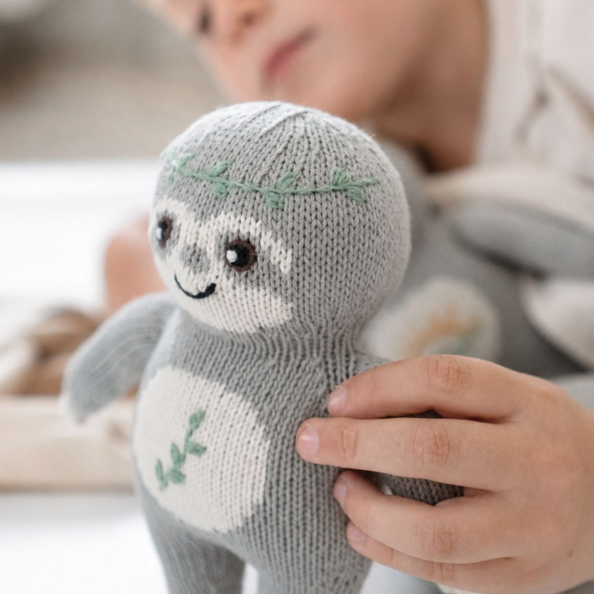 Kind hält das Baby Faultier Natur-Fauli aus Bio-Baumwolle mit grünen Blätterranken