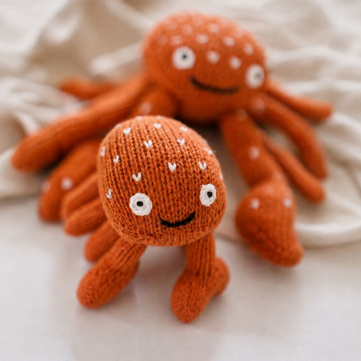 Kleines orangefarbenes Krabbe Kuscheltier Pablito vor einem großen gestrickten Krebs