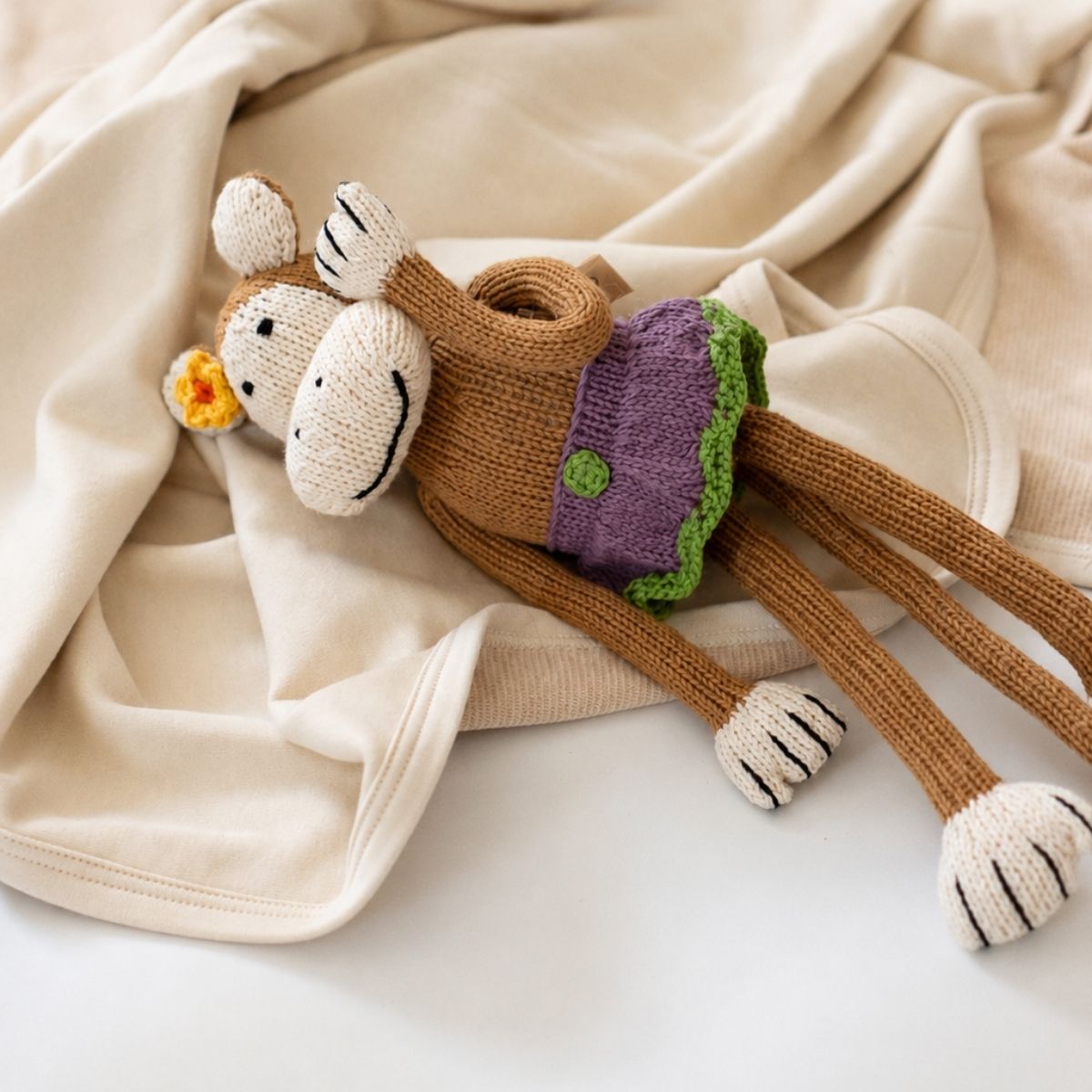 Braunes gestricktes Kuscheltier Affe mit lila Rock und gelber Blume auf hellem Stoff