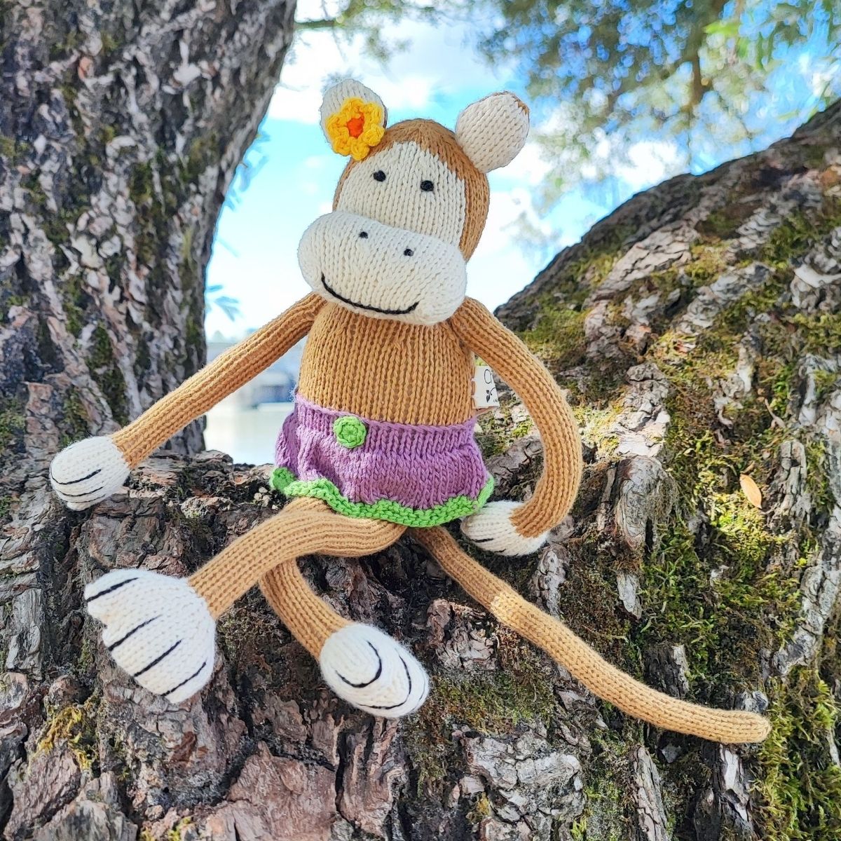 Handgestricktes Kuscheltier Affe Mädchen mit violettem Kleid in der Natur
