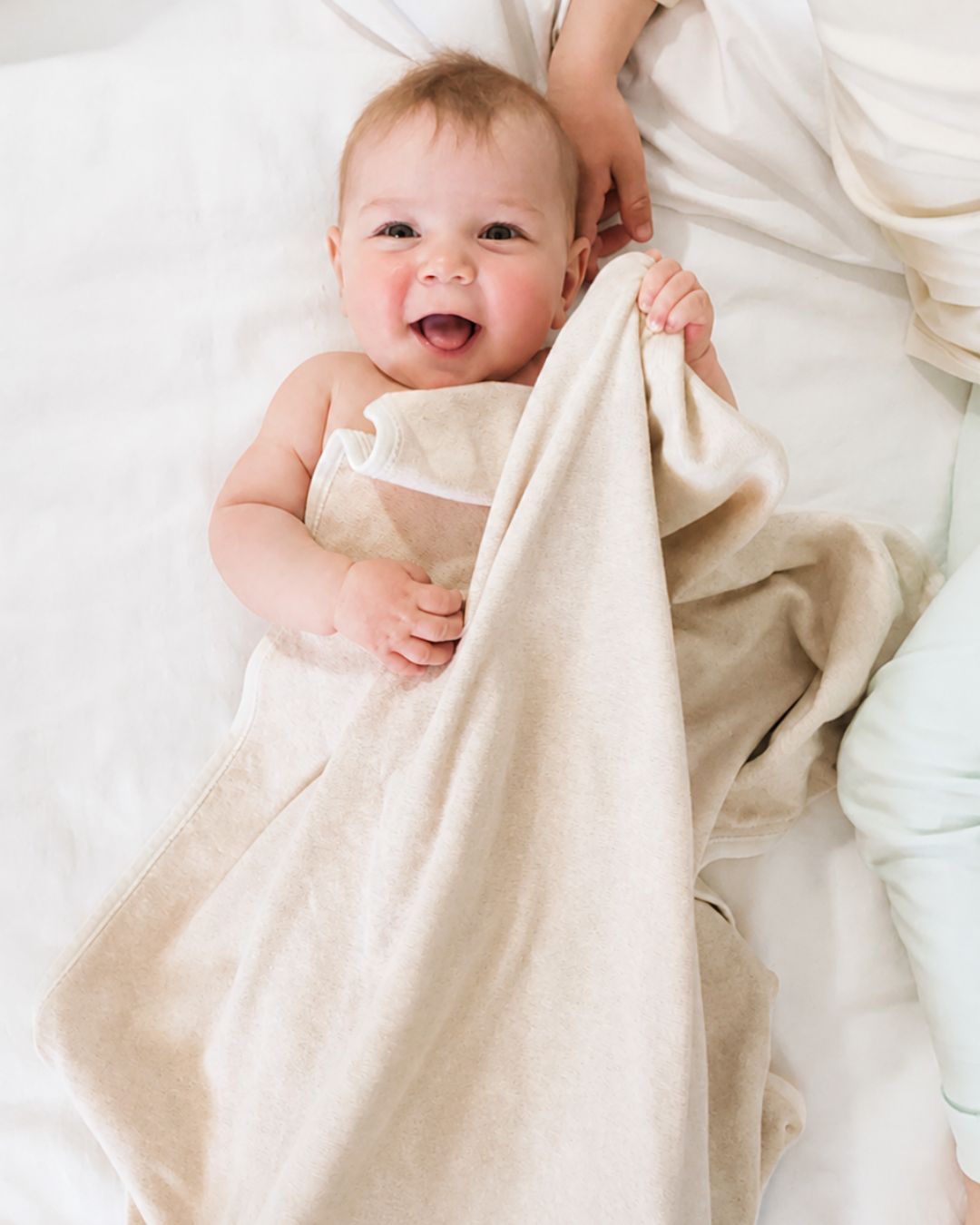 Baby liegt mit leichter Decke im Bett – Beispiel dafür, wie Eltern ihr Baby nachts richtig anziehen können