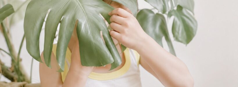 Kind versteckt sich hinter einer Monstera-Pflanze und trägt weiche Unterwäsche aus Pima Baumwolle bei sensorischer Empfindlichkeit