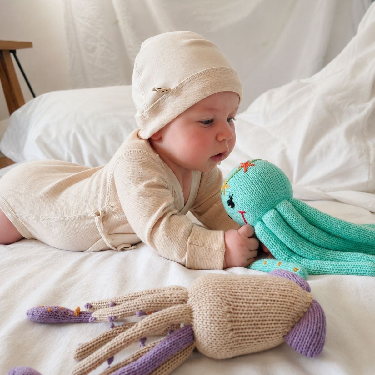 Neugeborenes im Sommer trägt Wickelbody und Mütze aus Bio-Pima-Baumwolle und spielt mit einem handgestrickten Oktopus
