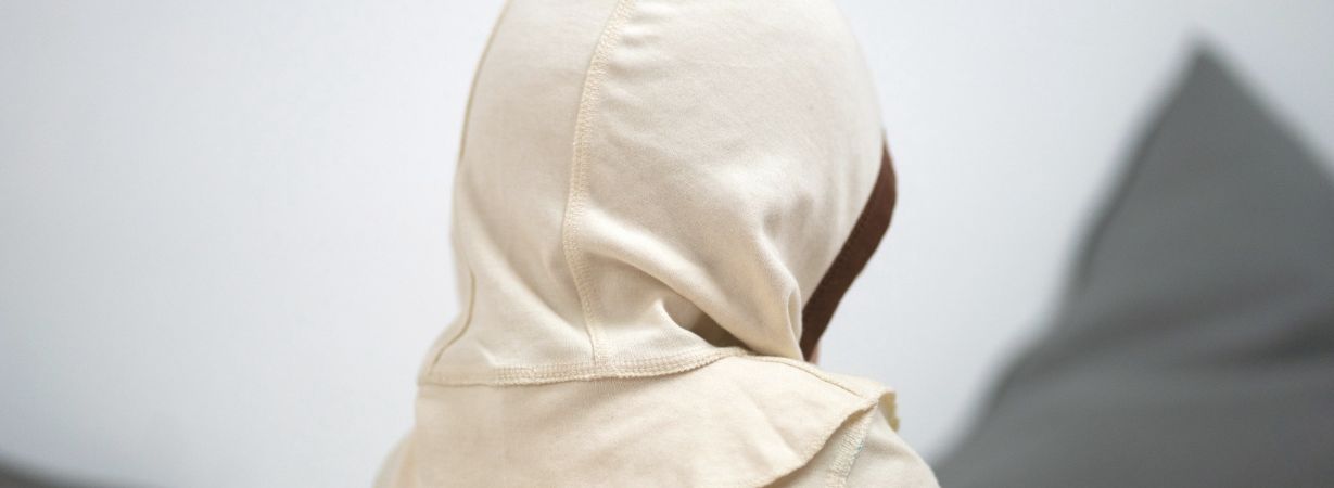 Kind mit Neurodermitis Kleidung sitzt abgewandt und verdeutlicht mögliche Anzeichen seelischer Belastung und Rückzug.