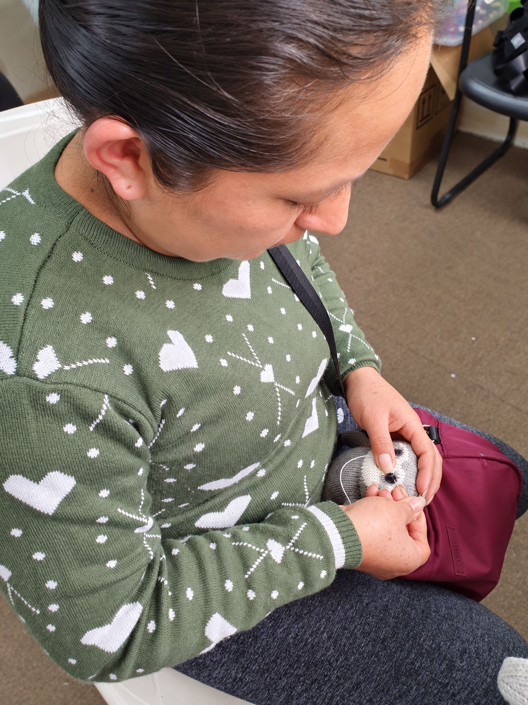 Handarbeiterin stickt mit Nadel und Faden das Auge eines gestrickten Faultiers in Lima