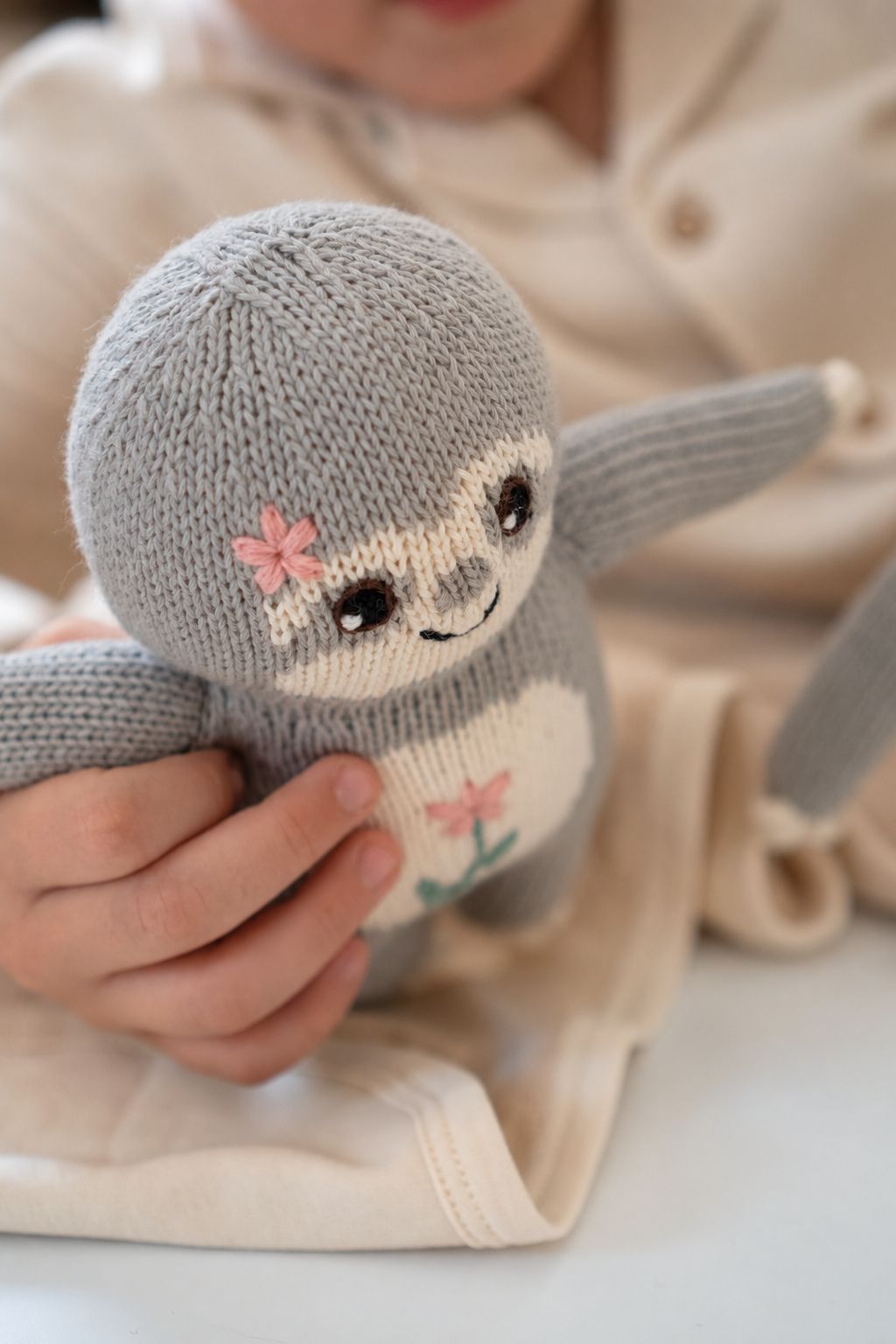 Kind hält ein handgestricktes Faultier mit aufgestickten Blumen in den Händen